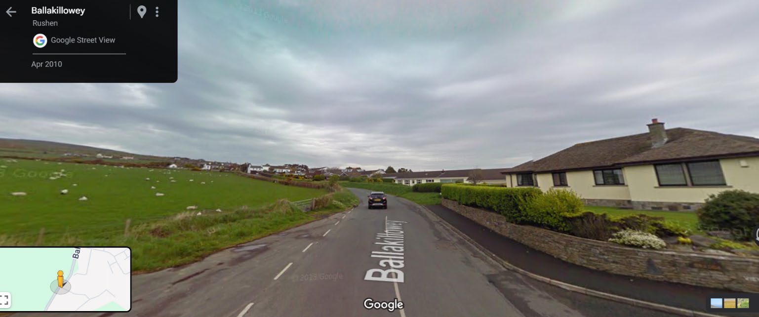 Google Street View screenshot showing a rural road scene with a detached bungalow on the right and green fields with sheep on the left.