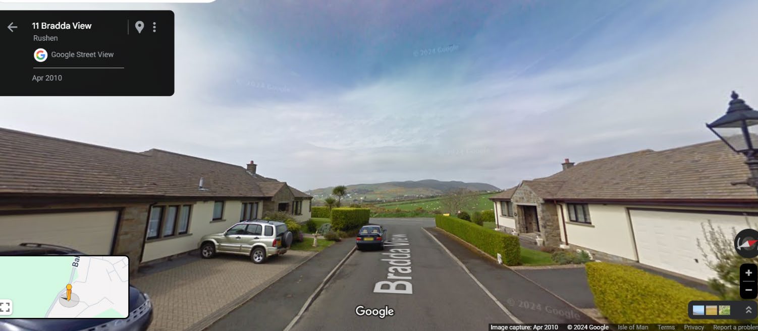 A Google Street View screenshot showing the residential street Bradda View in Rushen, featuring detached houses with garages and a view of hills in the background.