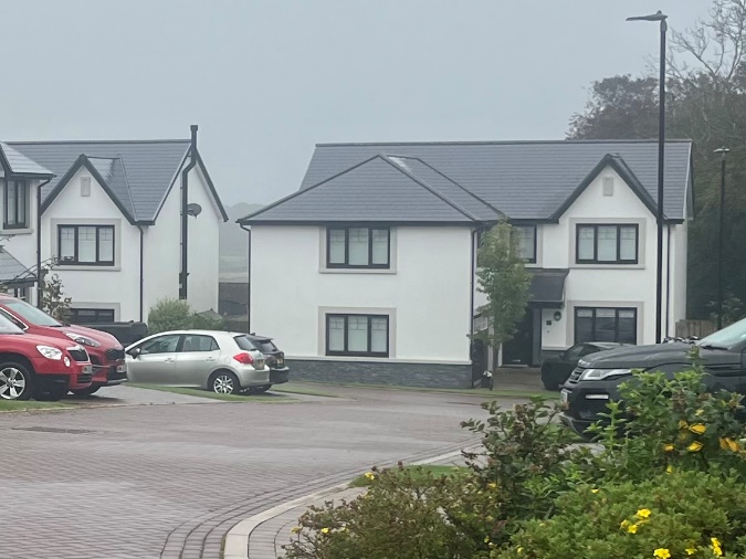 A photograph showing a row of modern white two-story houses with dark grey roofs on a residential street with parked cars.