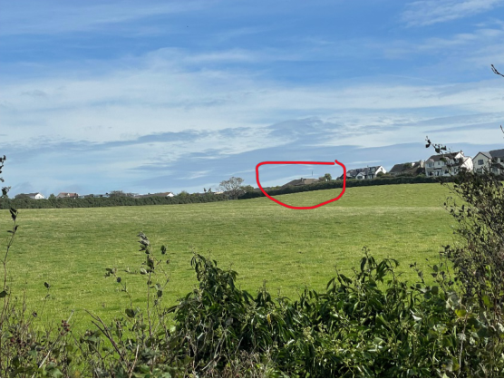 A landscape photograph showing a green field in the foreground with a row of houses on a hill in the background, highlighted by a red circle.