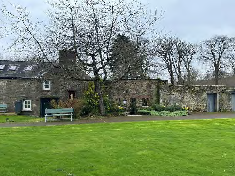 A photograph showing a stone building and adjacent wall structure with a grassy lawn in the foreground.