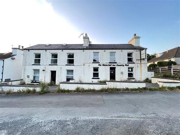 A street-level photograph of a white, two-story building identified as 'The Waterfall Inn Country Pub' situated in a rural setting.