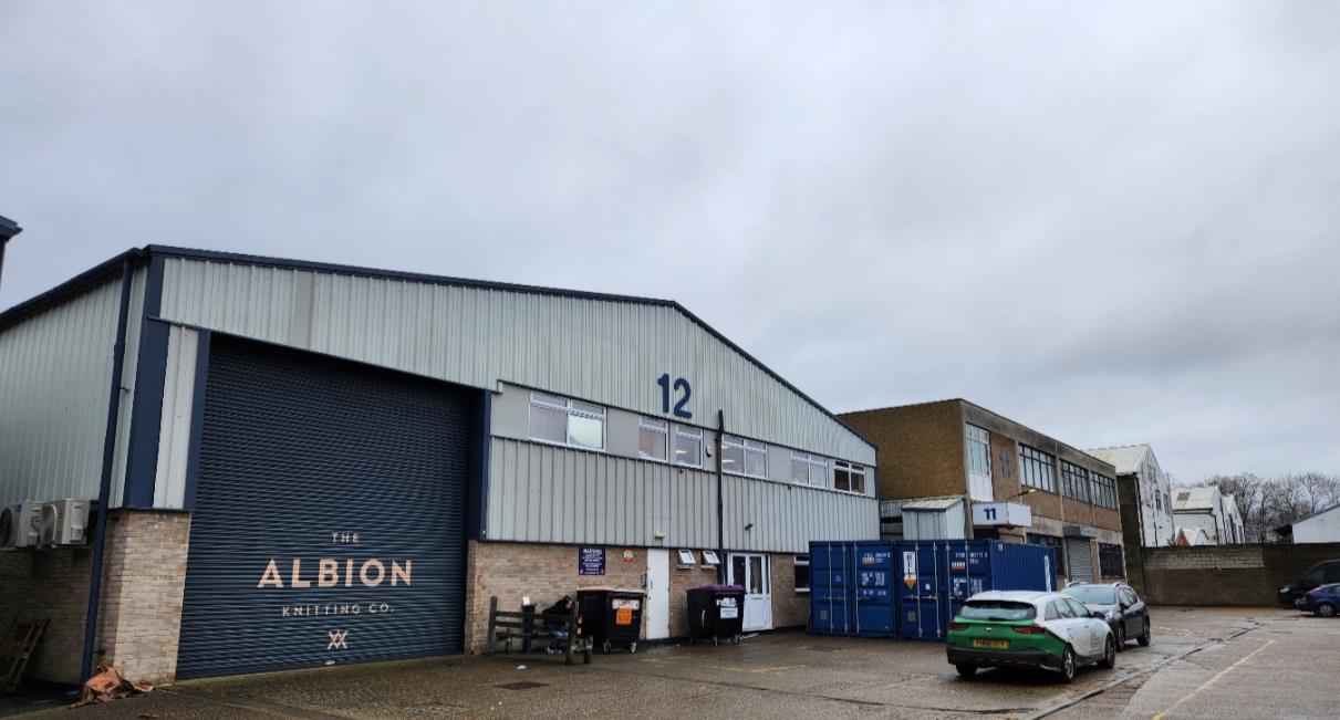 A photograph showing the exterior of an industrial unit, number 12, featuring a large roller shutter door with 'The Albion Knitting Co' branding and corrugated metal cladding.