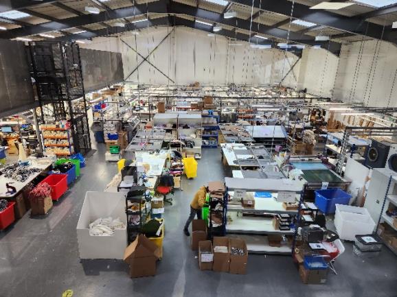 Interior photograph of a large industrial workshop or warehouse space featuring shelving, workbenches, and storage areas.
