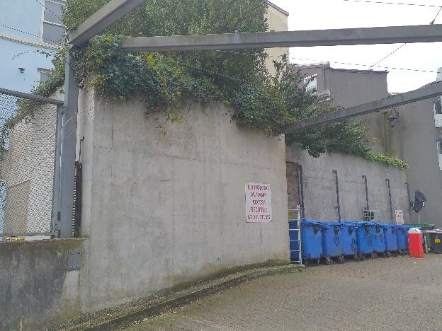 A photograph showing a concrete retaining wall with a 'Keep Clear' sign and a row of blue recycling bins in an urban setting.
