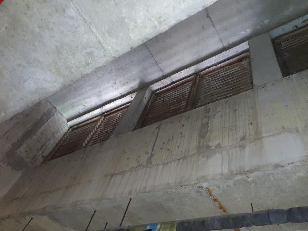 A tilted close-up photograph showing the underside of a concrete structure with wooden slatted vents and exposed rebar.