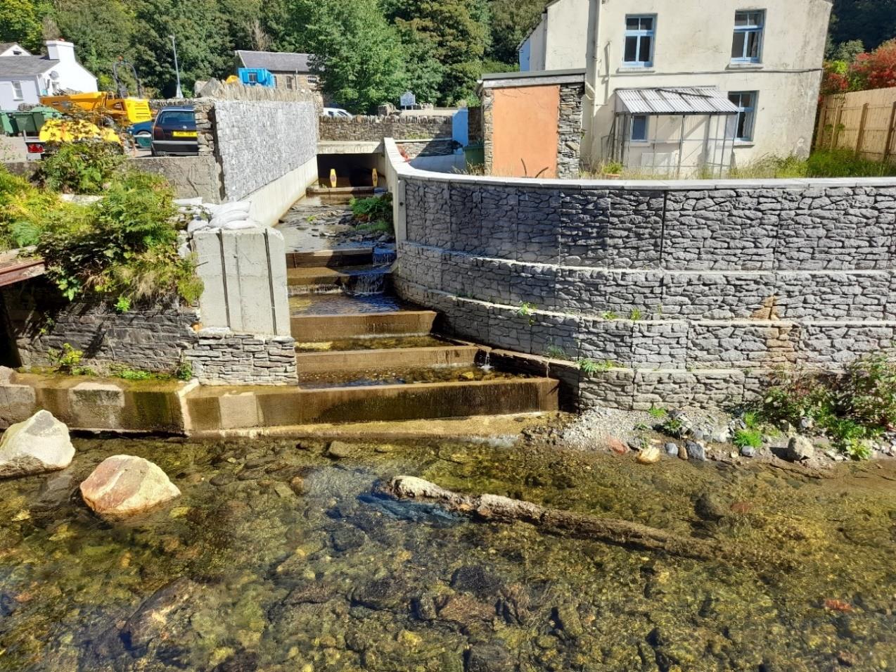 A photograph showing a constructed stone channel with stepped weirs for water flow, flanked by retaining walls.