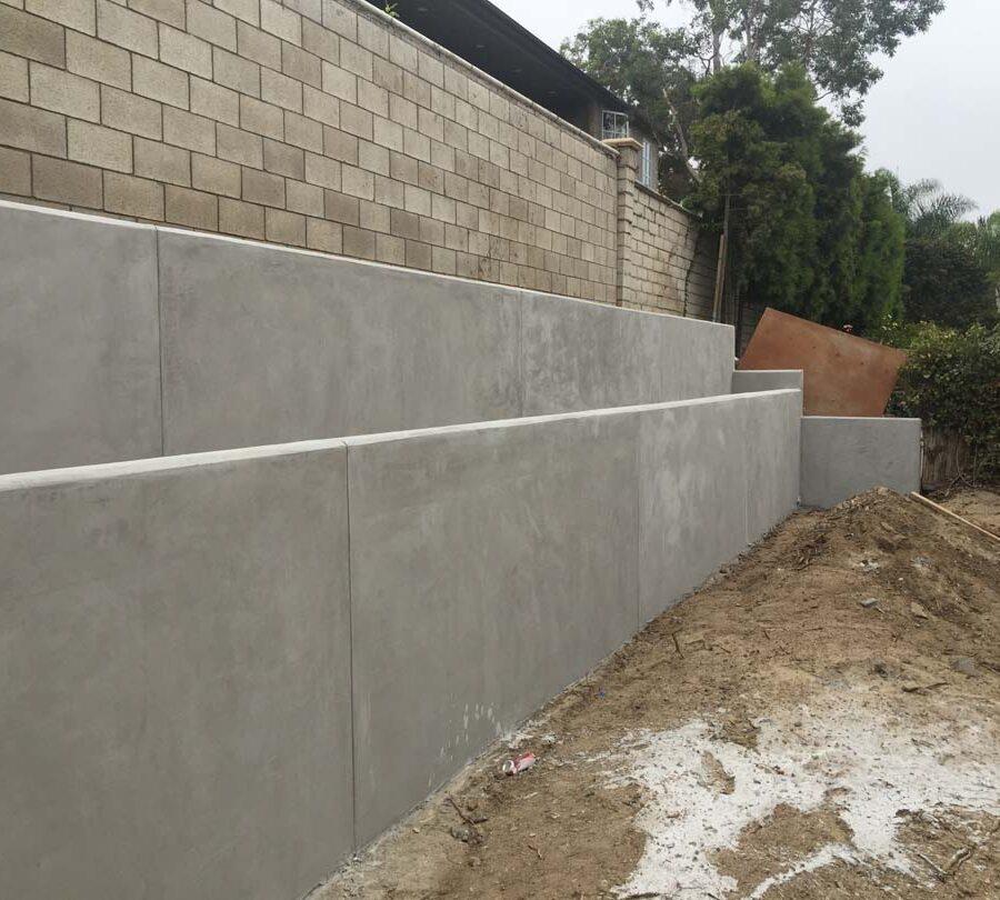 A photograph showing newly constructed tiered concrete retaining walls at a construction site with blockwork above.