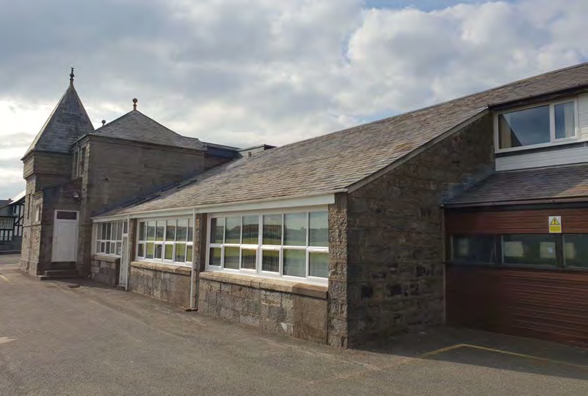 A photograph showing the exterior of a stone building with a slate roof and large white-framed windows, likely a converted barn or agricultural structure.