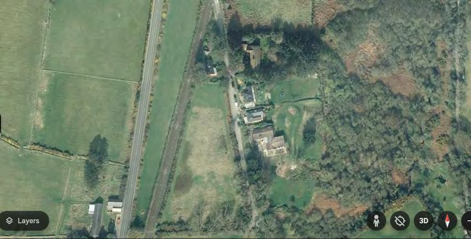 An aerial view of a rural site showing fields, a road, and existing buildings, likely used as a location map.