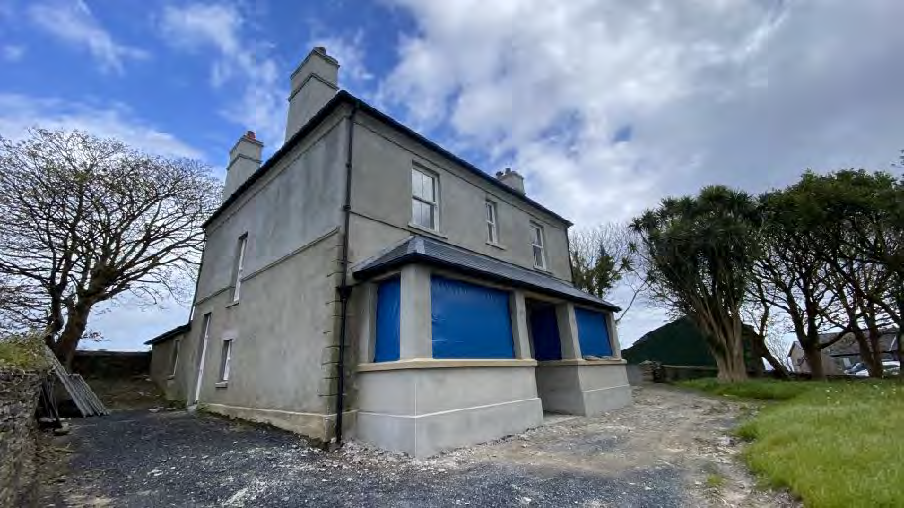A photograph of a two-story detached house undergoing renovation, featuring a single-story front extension with blue protective sheeting covering the openings.