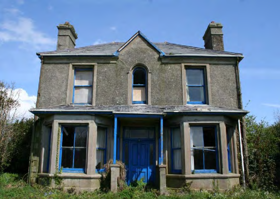 A photograph of a two-story detached house with pebbledash rendering and blue window frames, appearing to be in a state of disrepair or renovation.