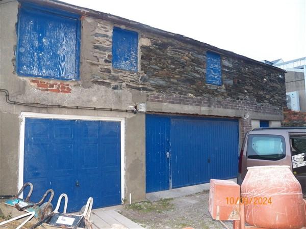 Exterior photograph of a stone and concrete building featuring large blue garage doors and boarded windows above.