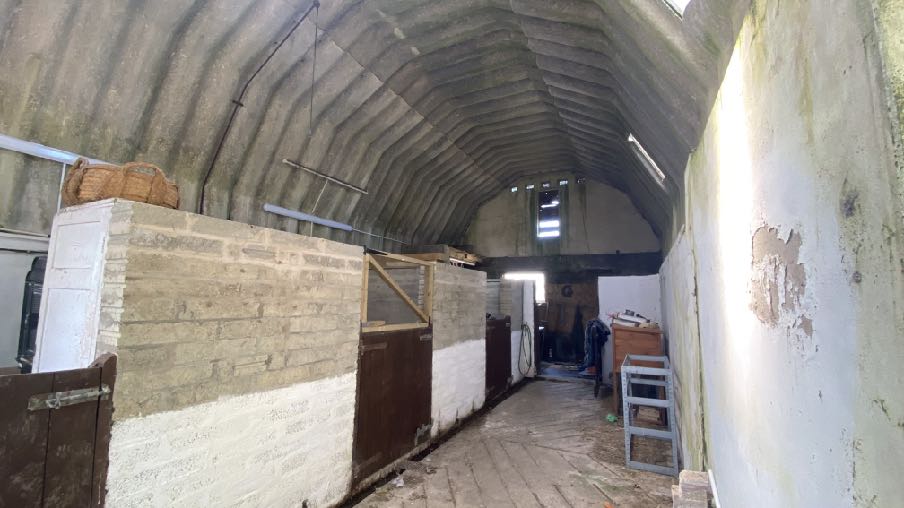 Interior photograph of a large outbuilding featuring a corrugated arched roof and brick stall partitions.