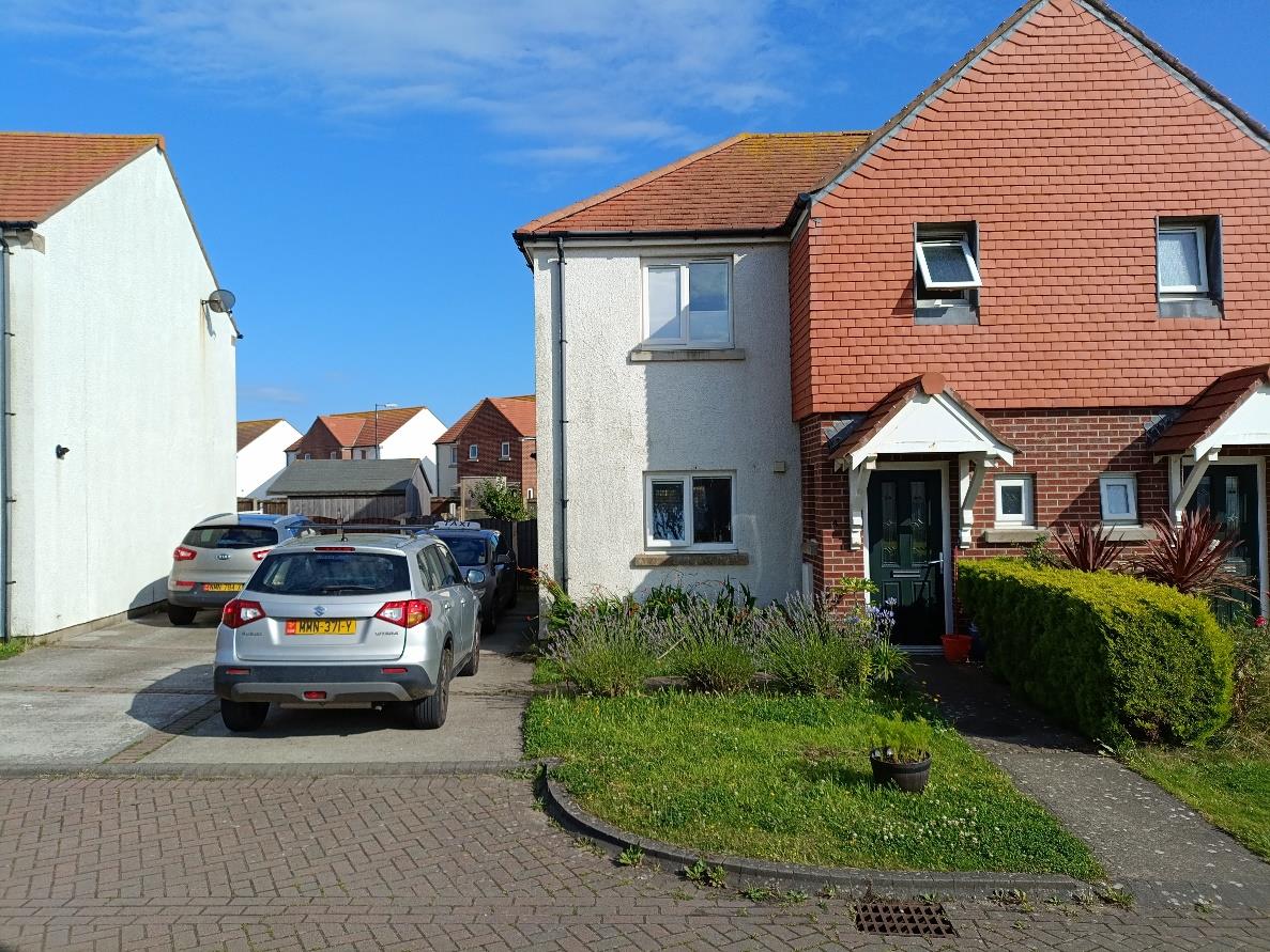 A street-level photograph showing a two-story residential property with red brick and white render cladding. The image includes a paved driveway with parked cars and a small front garden area.