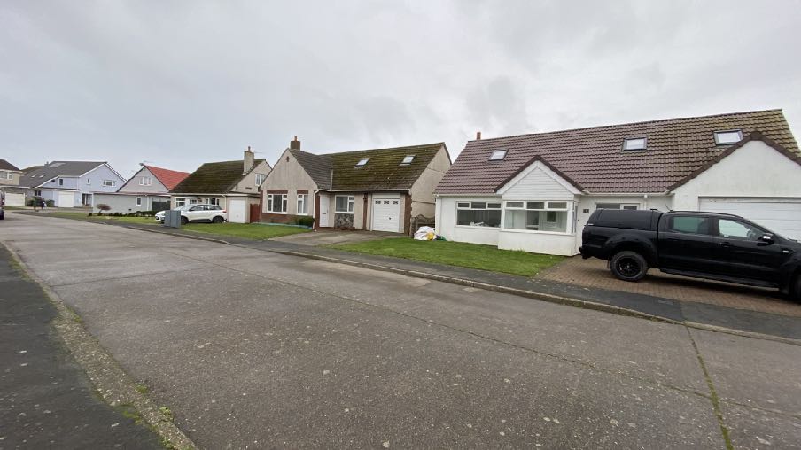 A street-level photograph showing a row of residential bungalows, focusing on a white house with an attached garage and a black pickup truck parked in the driveway.
