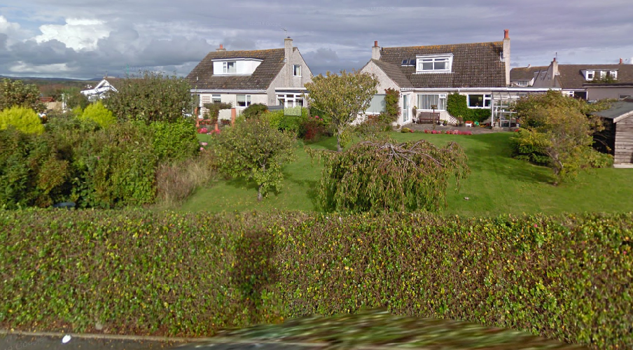 A photograph showing a view of two detached houses with gardens and hedges, likely serving as a site context image for the planning application.