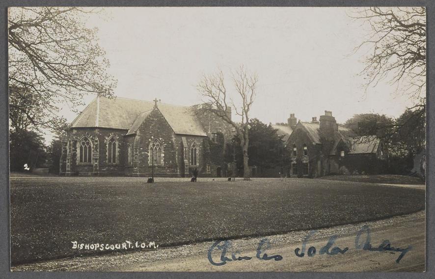 A vintage black and white postcard photograph showing a large stone building complex labeled 'Bishopscourt, I.O.M.' featuring a chapel-like structure and a residential building separated by a lawn.