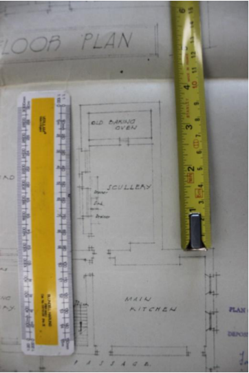 An architectural floor plan showing room layouts including a scullery and main kitchen, with rulers placed on top for scale.
