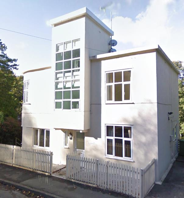 A photograph of a white, modern detached house featuring a tall vertical window section and a white picket fence.