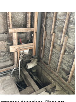 A photograph showing the interior of a building under renovation with exposed timber framing and stone walls, highlighting proposed drainage pipes.