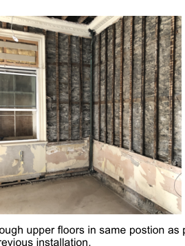 An interior photograph showing a room corner with a window and walls covered in vertical dark cladding or insulation strips.