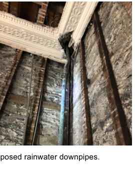 Interior photograph showing exposed brick walls and decorative cornicing with vertical pipes running down the wall, captioned 'proposed rainwater downpipes'.