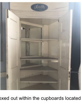 A photograph showing the interior of a white built-in cupboard with shelves and an open door.