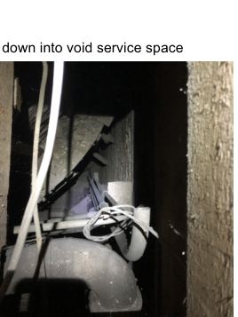 A close-up photograph showing the interior of a dark service void containing white PVC pipes and electrical cables.