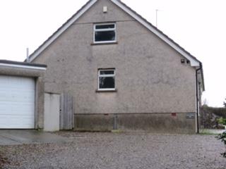 A photograph showing the exterior of a large, single-story agricultural building with a pitched roof, roughcast walls, and a white garage door.