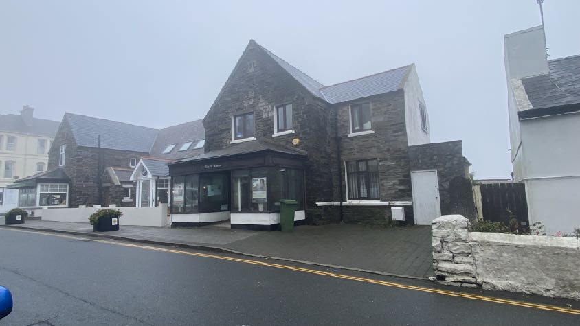 A street-level photograph of a stone building featuring a commercial ground floor frontage and residential upper storeys, set against a misty background.