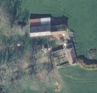Aerial photograph showing a rural site with a long agricultural building and adjacent structures in a green field.