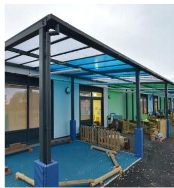 A photograph showing a newly installed steel canopy structure with a translucent blue roof attached to a building.