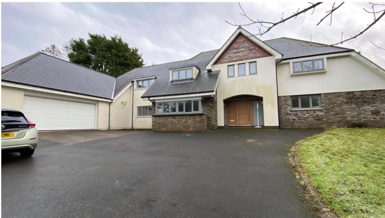 A photograph showing the front exterior of a large detached house with an attached garage and paved driveway.