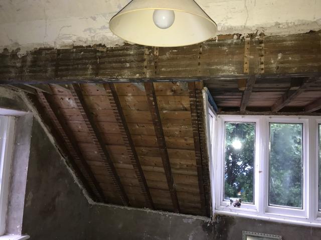 Interior photograph of a room under renovation showing exposed wooden roof rafters and a steel support beam.