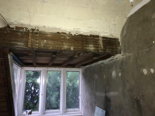 Interior photograph of a room under construction or renovation, featuring exposed wooden ceiling beams and unfinished walls.