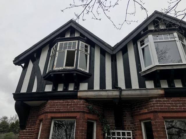 A low-angle photograph of an existing two-story house featuring black and white half-timbering on the upper level and red brick below.