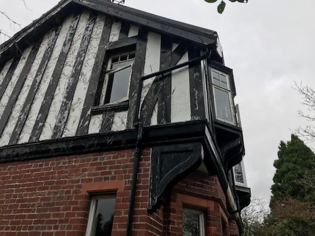 A low-angle photograph showing the corner of an existing residential property with a red brick ground floor and a black-and-white half-timbered upper story.