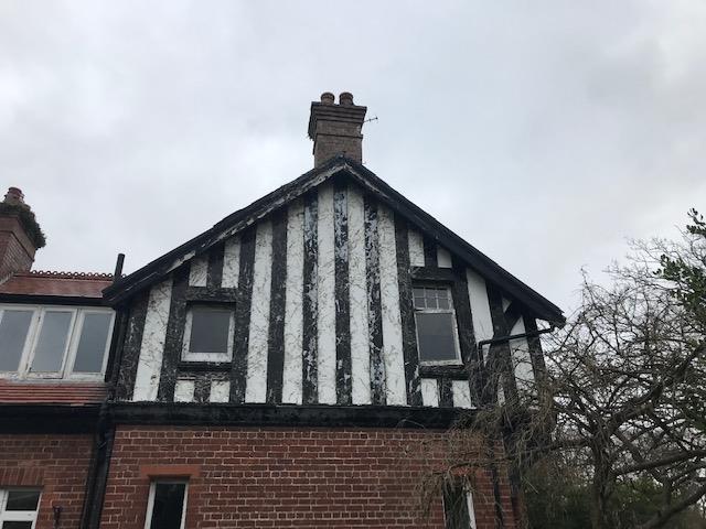 A low-angle photograph showing the gable end of a residential property featuring black and white timber framing above red brickwork.