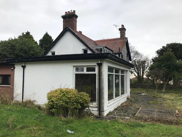 A photograph of a white single-story detached bungalow featuring a large glass conservatory extension and a grassy front garden.