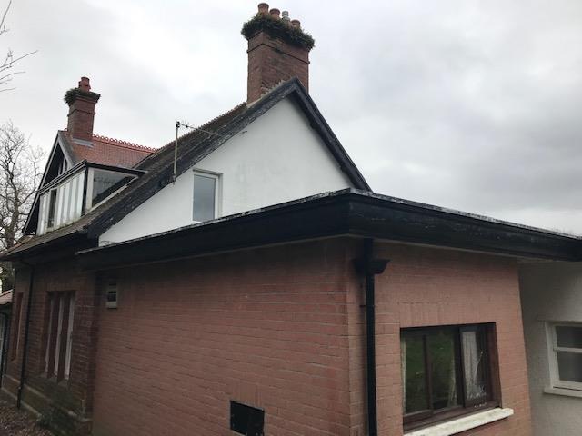 A photograph showing the exterior of a single-story red brick house with a pitched roof and chimneys.