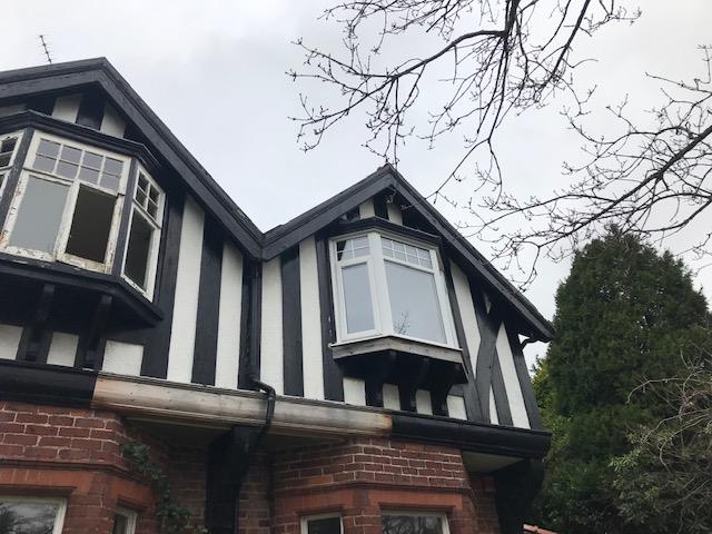 A low-angle photograph showing the upper facade of an existing two-story house with black and white timber framing and bay windows.