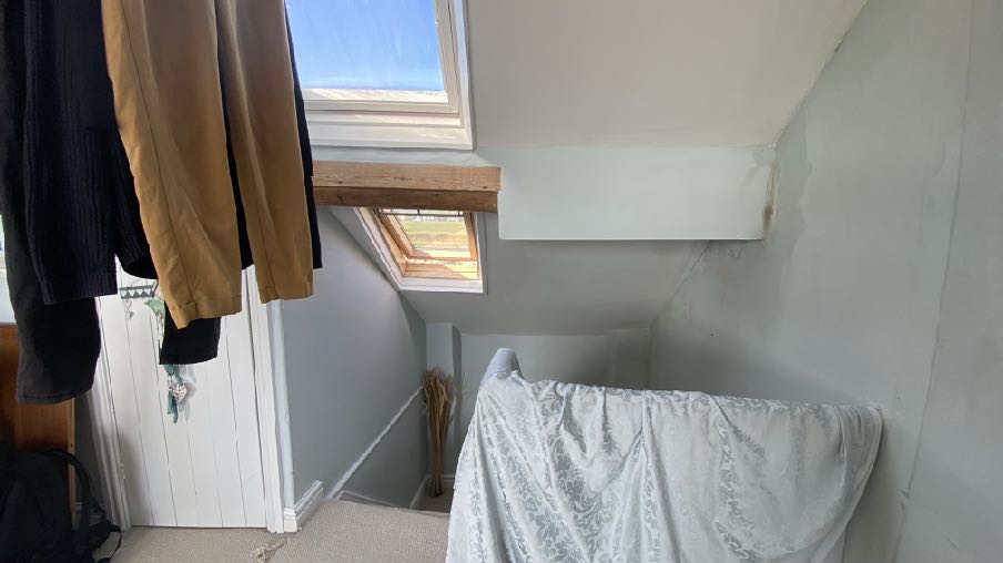 Interior photograph of a loft conversion space featuring sloped ceilings, skylights, and a wooden beam.