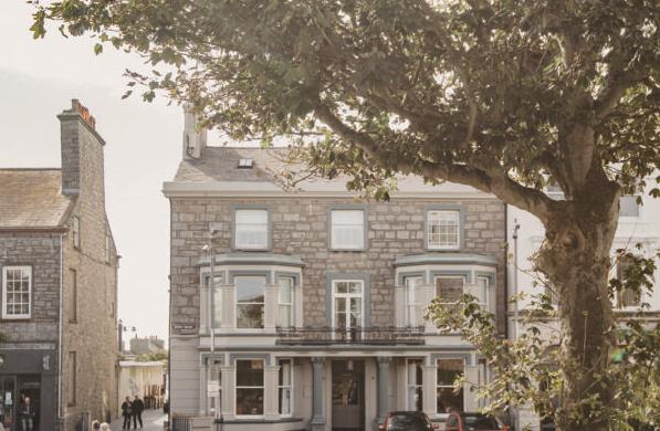 A street-level photograph of a two-story stone building with bay windows, partially obscured by a large tree in the foreground.