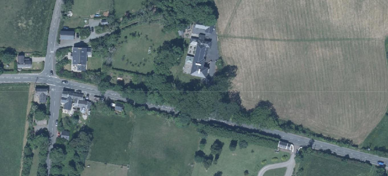Aerial satellite view of a rural property showing a large building complex situated near a road junction and surrounded by agricultural fields.