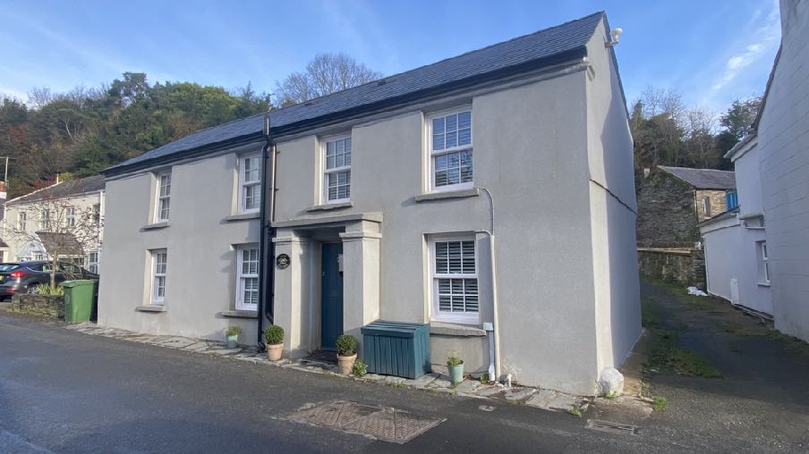 A street-level photograph of a two-story, rendered residential building with a slate roof and white sash windows.