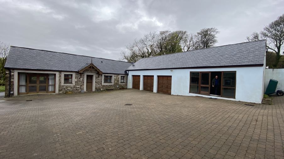 A photograph showing the exterior of a single-story property featuring a stone section and a white section with three garage doors and a large paved driveway.