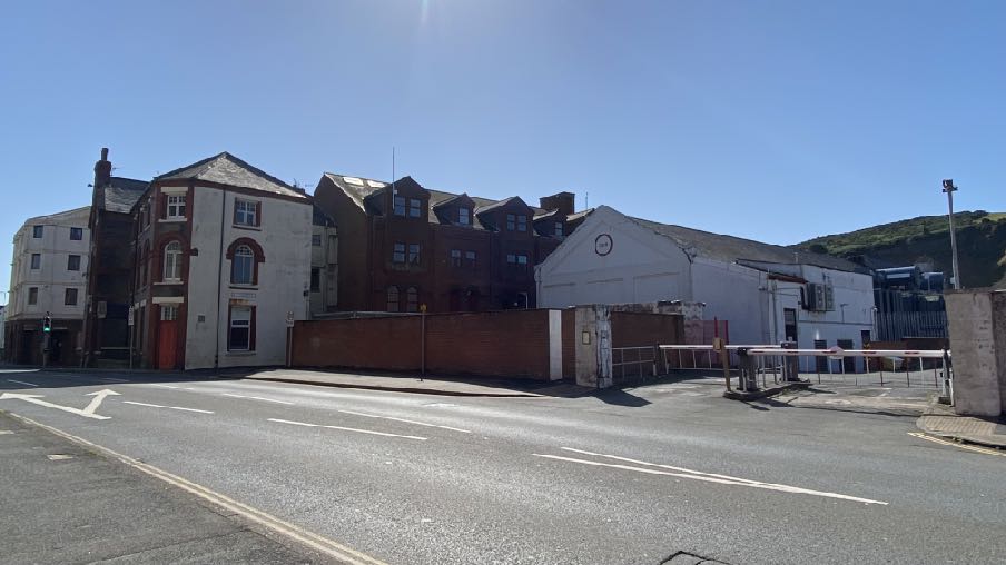 A street-level photograph showing a row of commercial and industrial buildings along a road in Douglas, featuring a gated entrance and barrier.