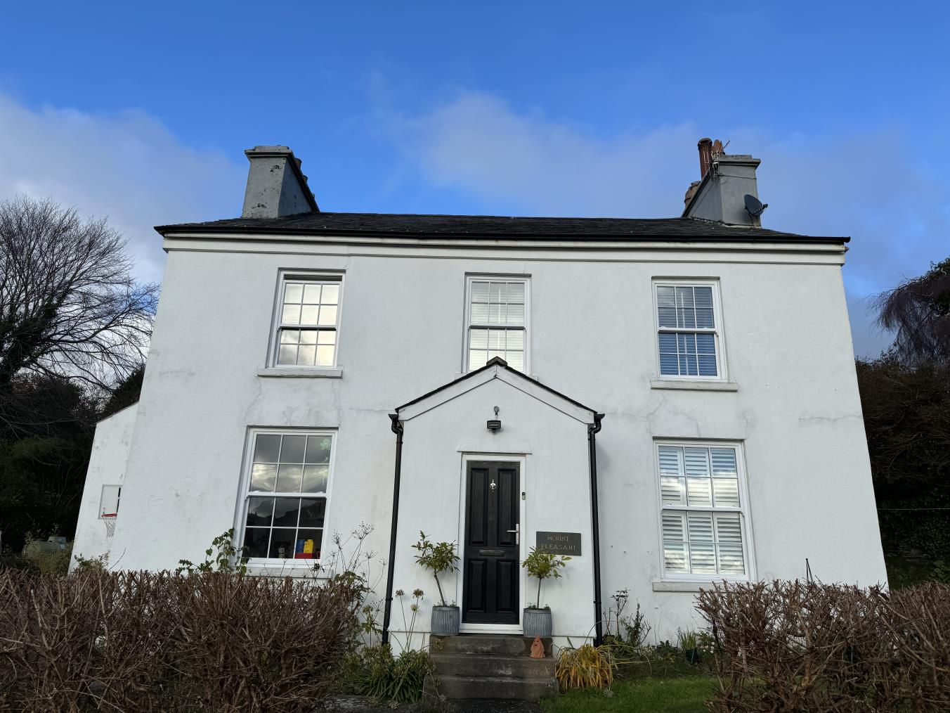 A photograph showing the front elevation of a white, two-story detached house with a central entrance porch and sash windows.