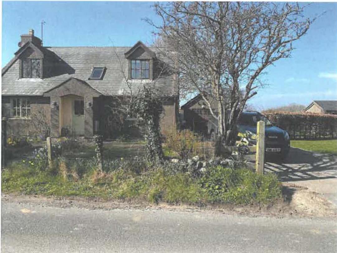 A photograph showing a detached stone cottage and an adjacent outbuilding or stable block in a rural setting.